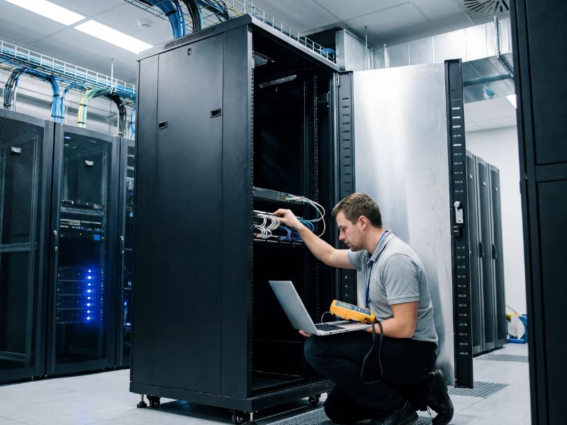 Technician with laptop testing cabling inside an open Zatech cabinet in a server room